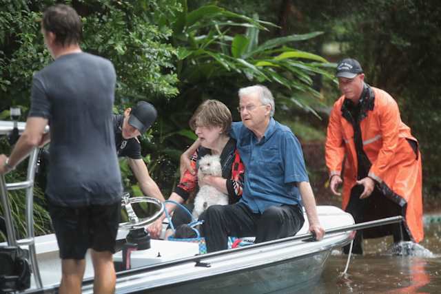 Here, an elderly woman clings to her poodle as the whole family is rescued by an emergency crew.