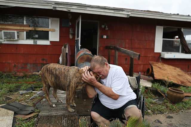 A man holds his dog and weeps outside the wreckage of their home.