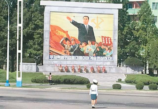 Traffic ladies em frente a uma da tantas propagandas do regime na capital da Coreia do Norte 